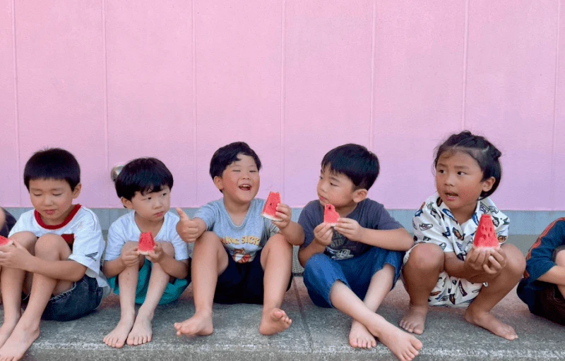 年長の男の子たちが幼稚園で笑いながらスイカを食べている様子