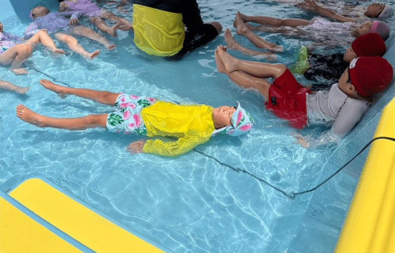 幼稚園のプールで仰向けになり目をとじて浮かぶ年長さん