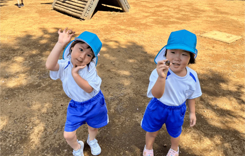 年少の女の子2人がどんぐりを持って嬉しそうに笑っている様子