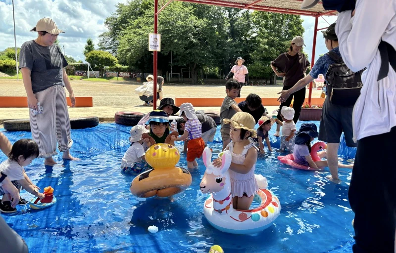水着を着た複数の2歳児がプールで浮き輪を持って水遊びを楽しんでいる様子