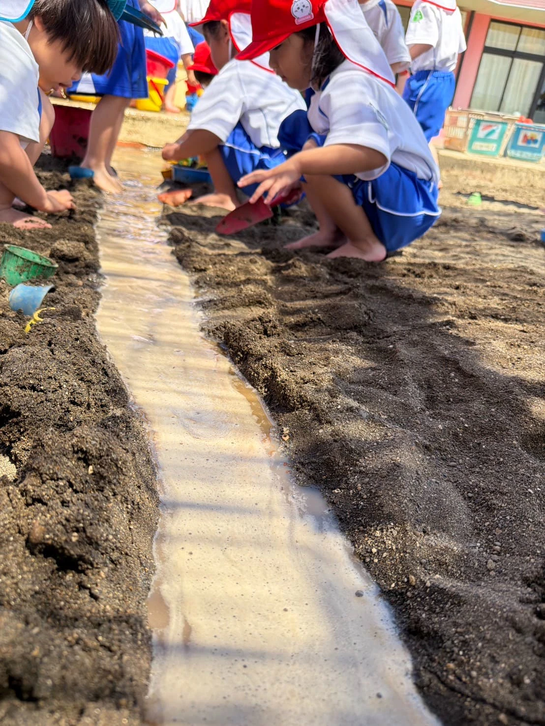 みもみ幼稚園の砂場に水を流し川が出来ている様子