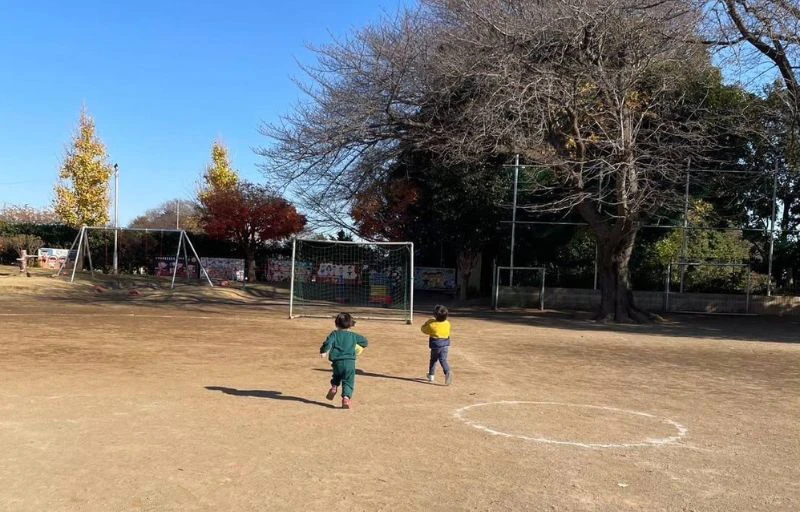 2歳の男の子二人が幼稚園の園庭でサッカーボールを持って走っている様子