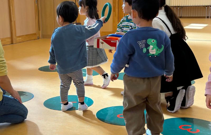 複数の2歳児が、数字マットの上で輪投げを持って遊んでいる様子