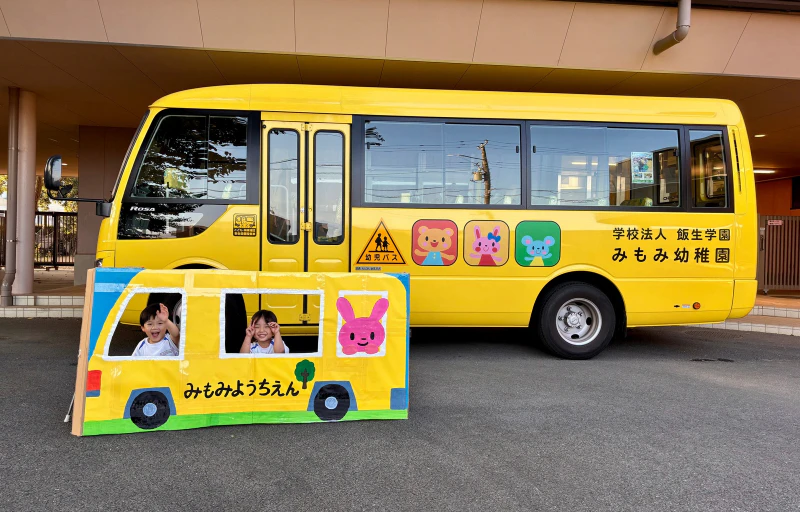 幼稚園の黄色い園バスの前で同じバスの形をした顔はめパネルから顔を出して笑顔を見せる女の子と男の子