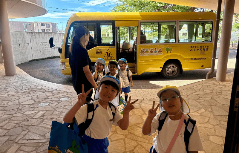 幼稚園バスから降りた女の子二人がカメラに向かってピースしている様子