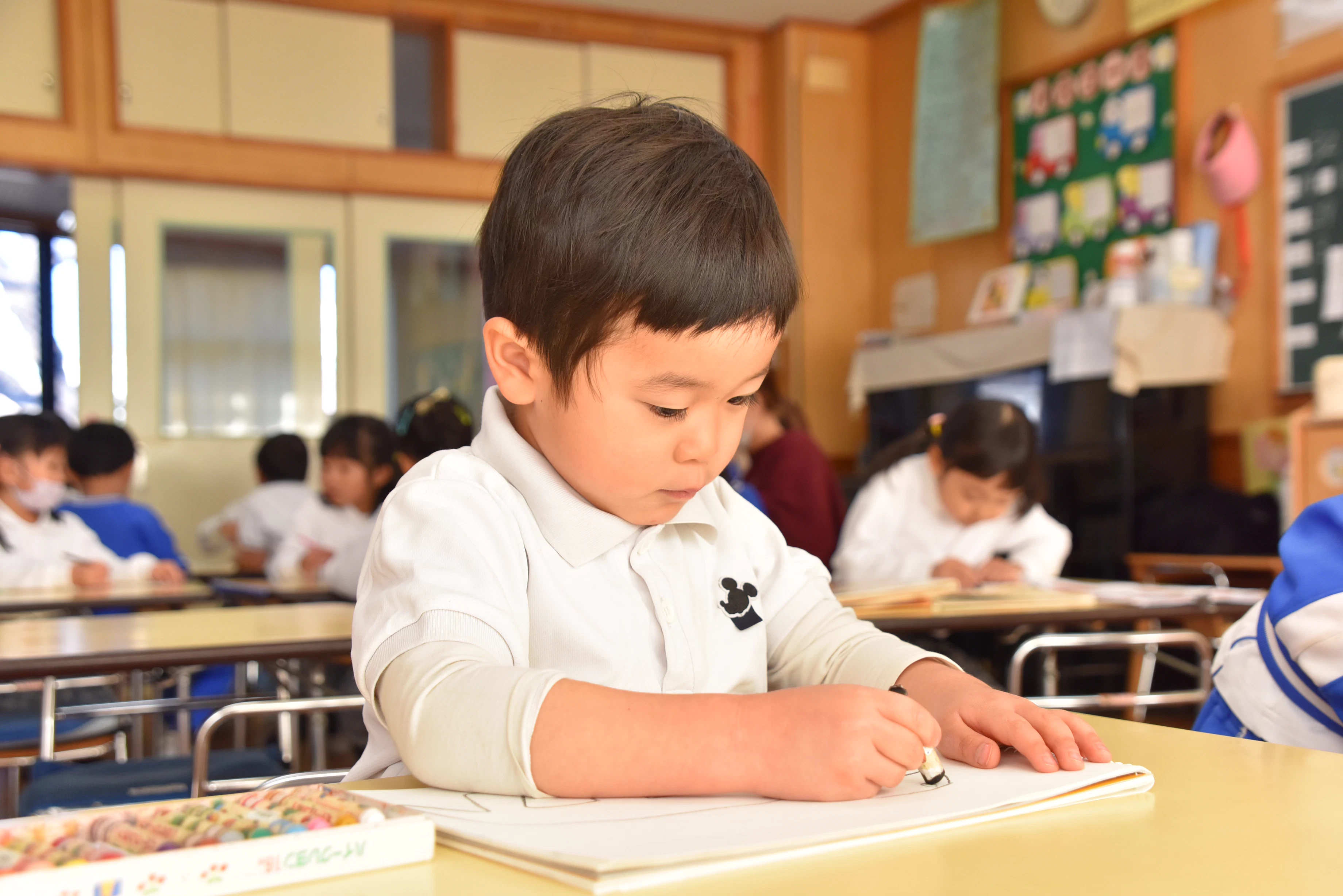 5歳の男の子が集中して画用紙に絵や文字を描いている様子