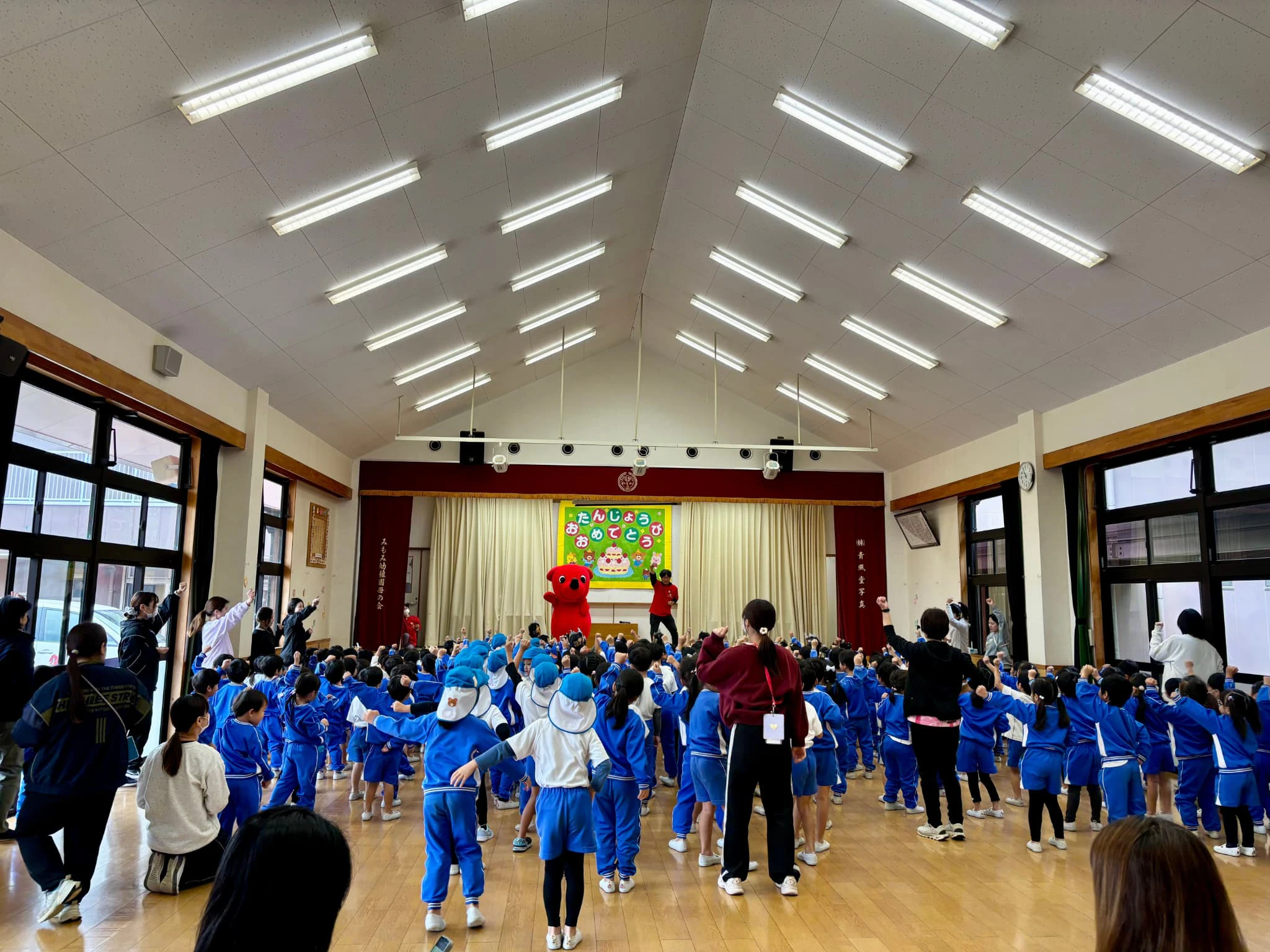 チーバくんが幼稚園のホールで園児たちとダンスを踊っているところ