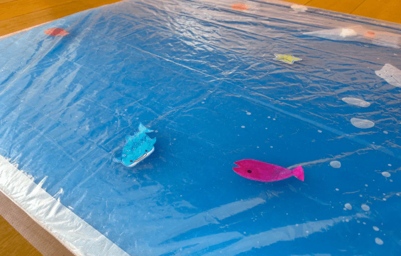 圧縮袋に水や魚のおもちゃを入れた3歳児が3人ほど寝っ転がれる大きさの手作りウォーターマット