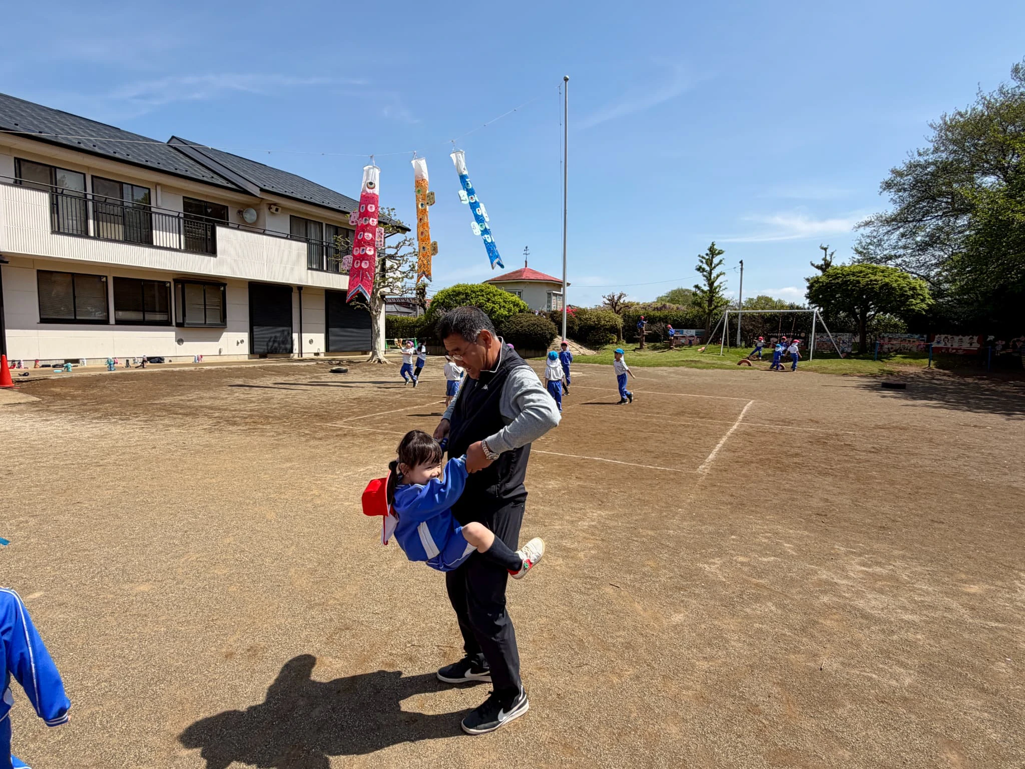 園庭で泳ぐ鯉のぼりと副園長先生に抱っこしてもらう女の子