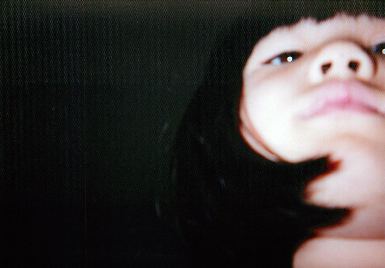 暗い背景の中で、幼い女の子の顔の下部分がアップで写っている写真