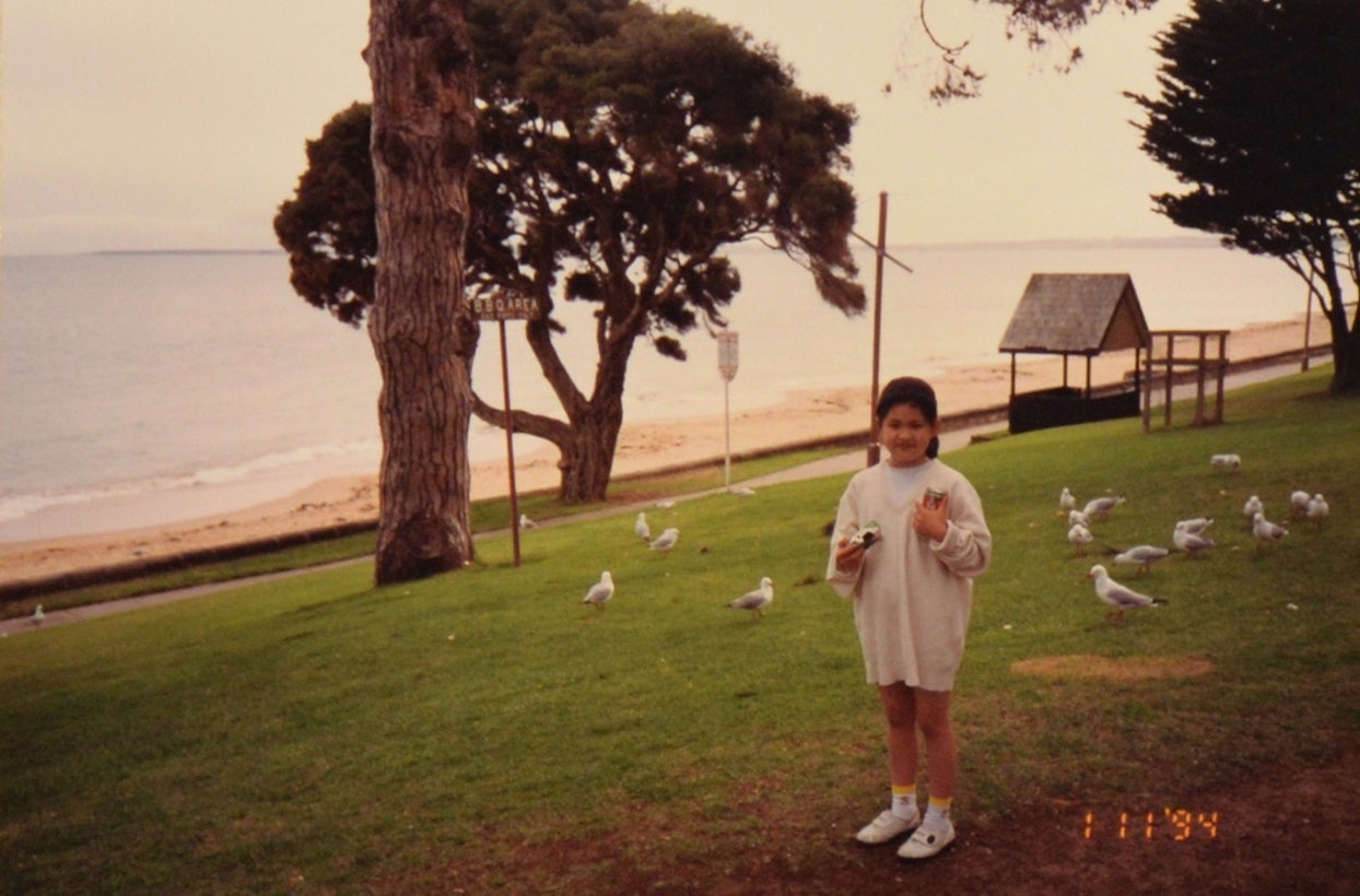 海辺で鳥たちに囲まれて立つ少女。手には「写ルンです」を持っている。1994年の日付スタンプがある。