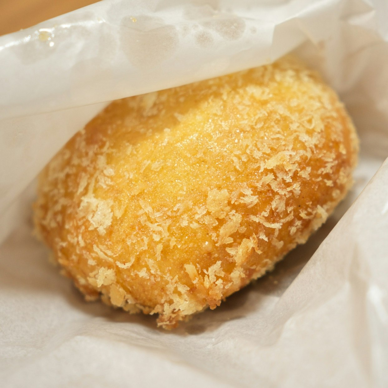揚げたてのきつね色のカレーパンが白い紙袋に包まれている接写画像。パン粉の衣がはっきりと見える。
