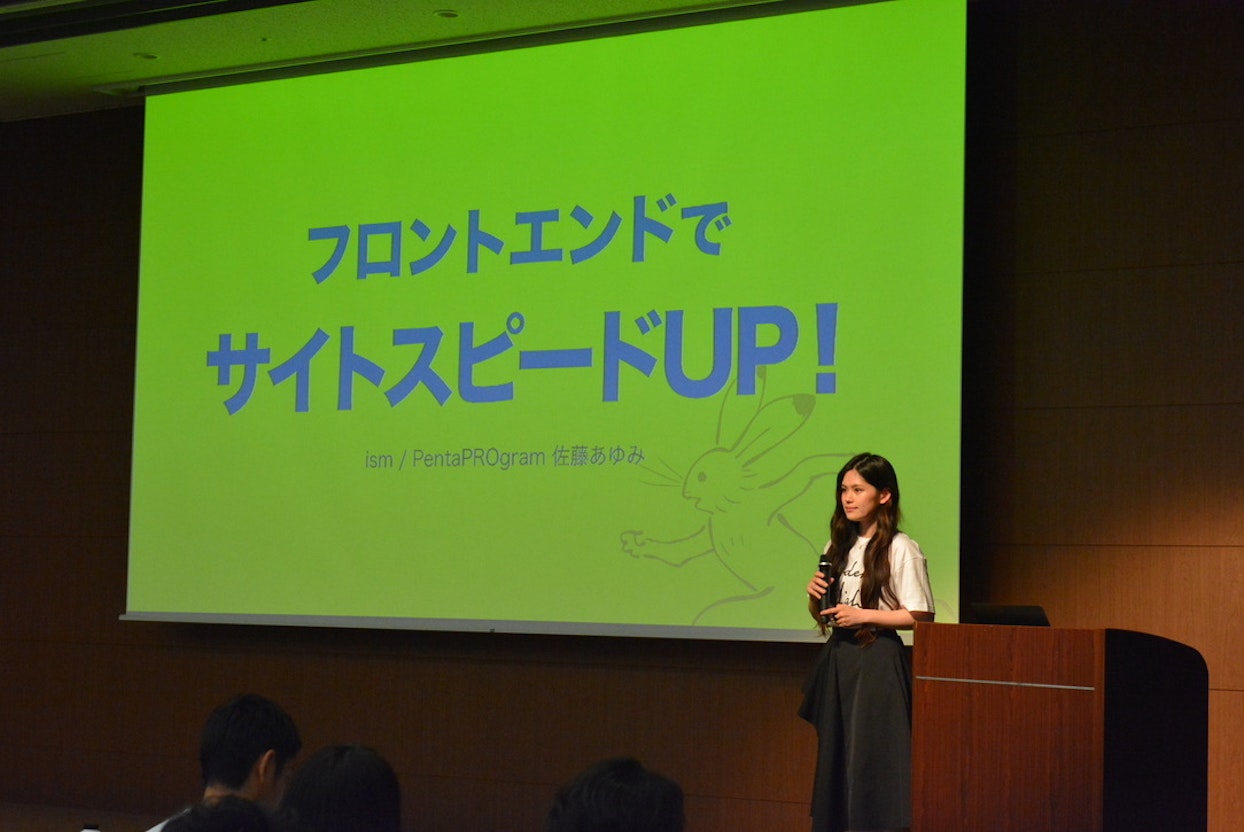 フロントエンドでサイトスピードUP!のスライドを投影したスクリーンの前に立つ女性