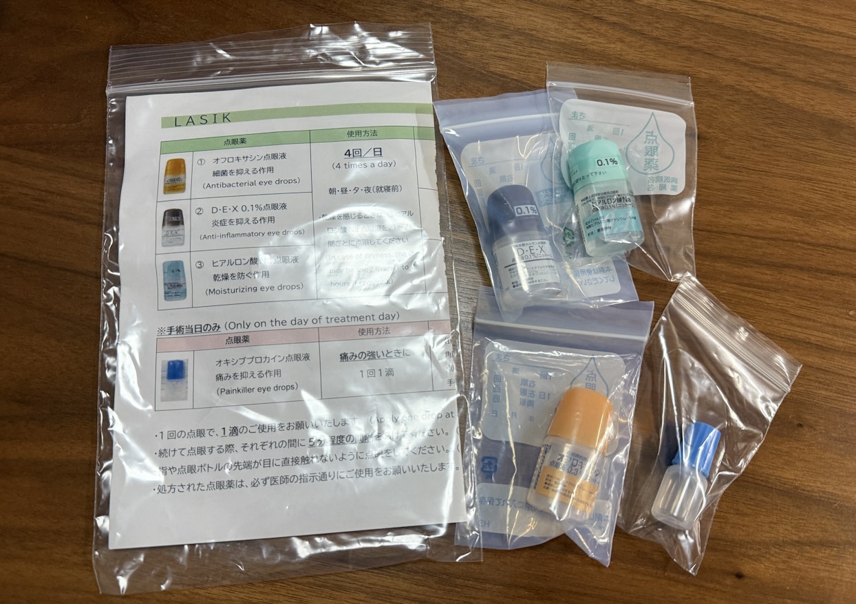 木製のテーブルの上に置かれた、LASIK手術後の点眼薬セット。4種類の点眼薬と使用方法が書かれた説明書がクリアな袋に入っており、点眼薬のボトルもそれぞれの袋に小分けにされている。