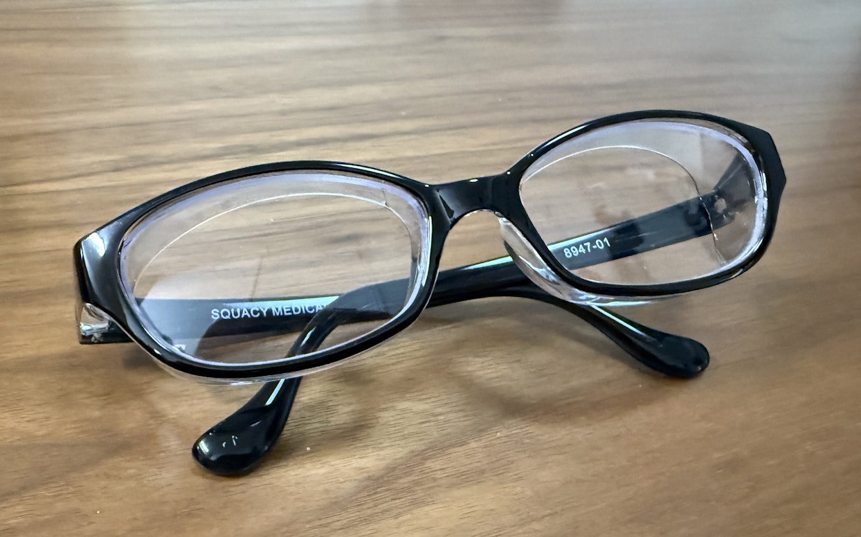  木製のテーブルの上に置かれた黒いフレームのメガネ。