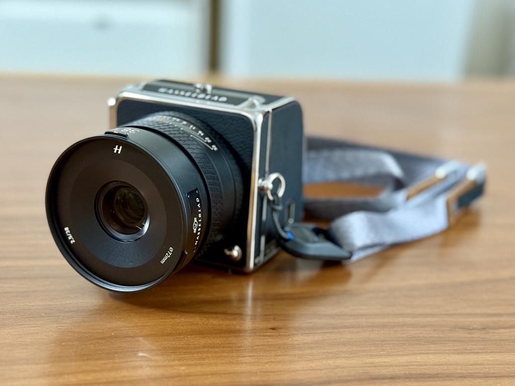 木製のテーブルの上に置かれた、レンズと灰色のストラップが付いたクラシックなデザインのHasselblad中判カメラ