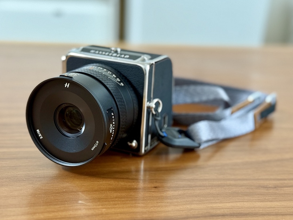木製のテーブルの上に置かれた、レンズと灰色のストラップが付いたクラシックなデザインのHasselblad中判カメラ