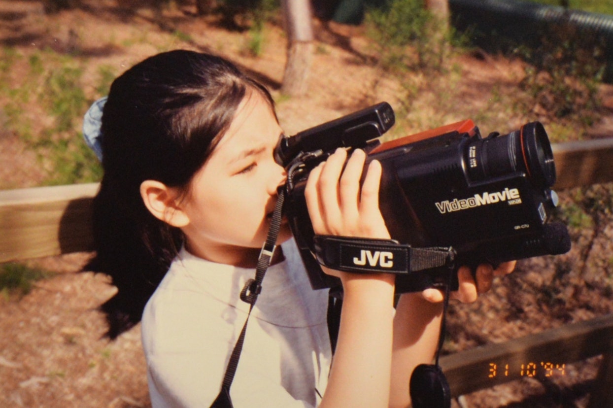屋外で大きなJVCのビデオカメラを使用している少女。1994年の日付スタンプがある。