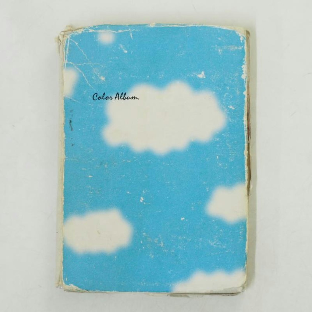 青空と白い雲が描かれた古い「カラーアルバム」の表紙。表紙は擦り切れや汚れが見られる。