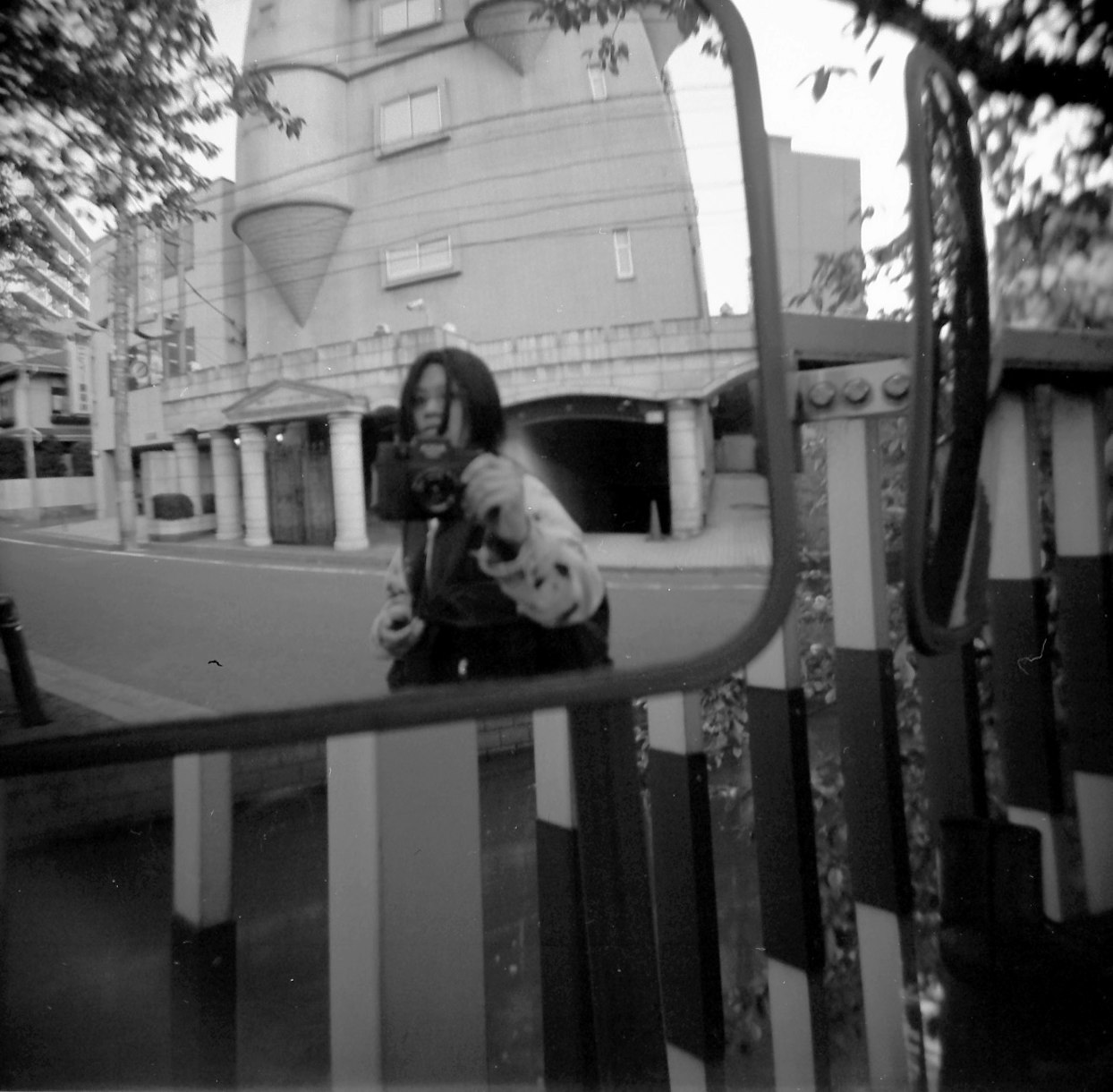 通りに面した建物の前で、道路のミラー越しに写真を撮っている人物の白黒画像