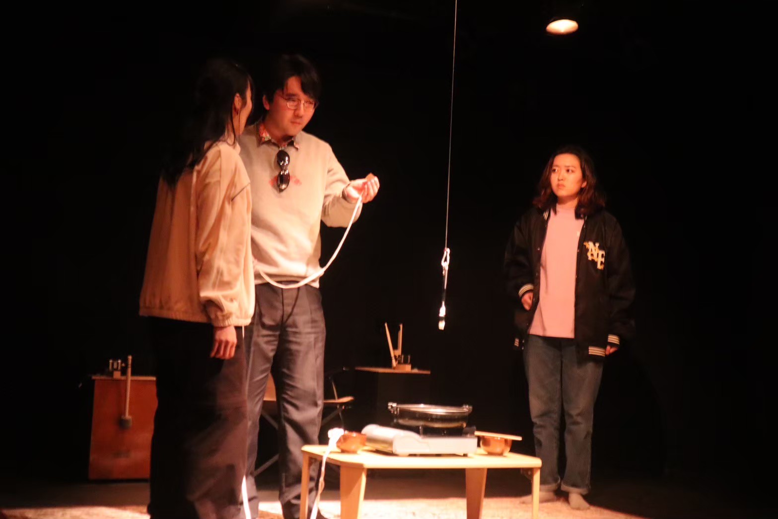 吉報 vol.3での「すき焼きにマジックマッシュルーム入れんな!」上演写真。出演者のうめだ、小島光生、小藤琴が天井からつり下がった虫眼鏡を見つめている。虫眼鏡の下にはローテーブルがあり、すき焼きの用意がされている。