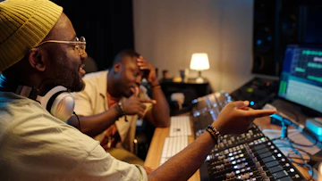 男性二人がパソコンの画面を見ながら音楽制作を行っている