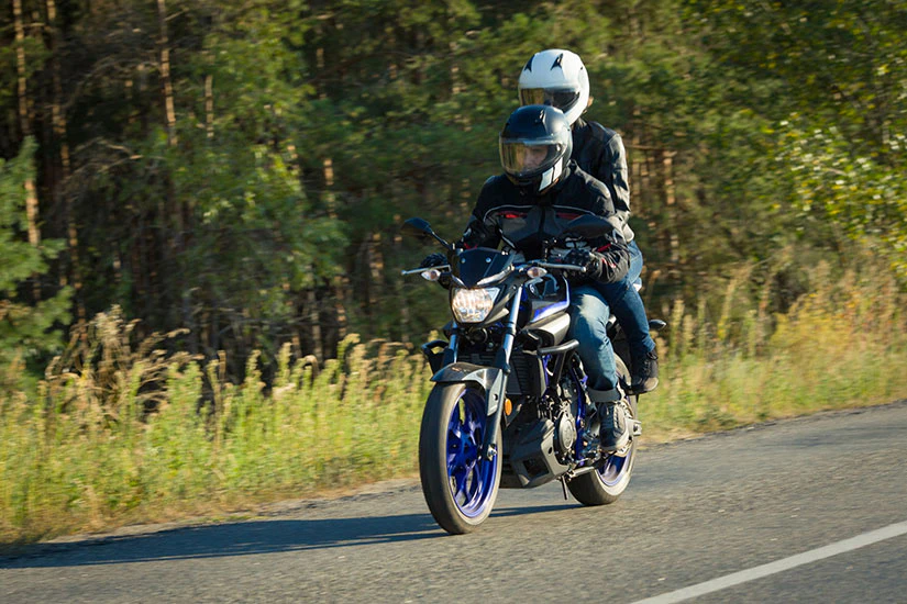 森の中の道をバイクで二人乗りしている様子の画像