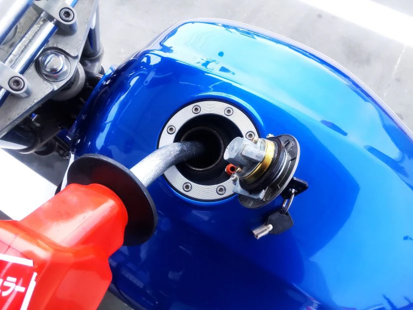 青いバイクのガソリンタンクに赤い給油ノズルを差し込み、給油している様子。給油口のキャップは開けられている。