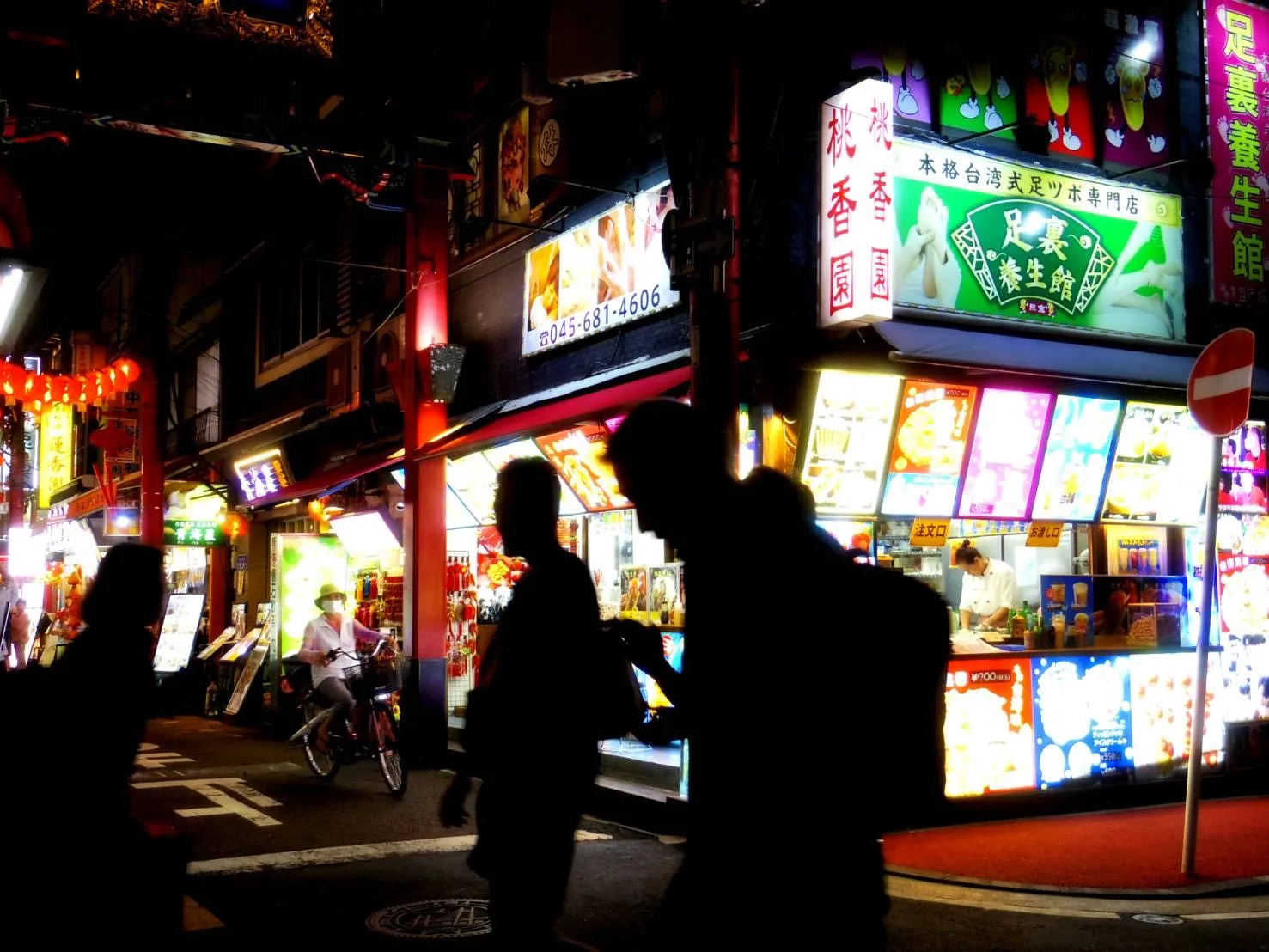 夜の中華街の看板の光を背景に通行人がシルエットで写っている