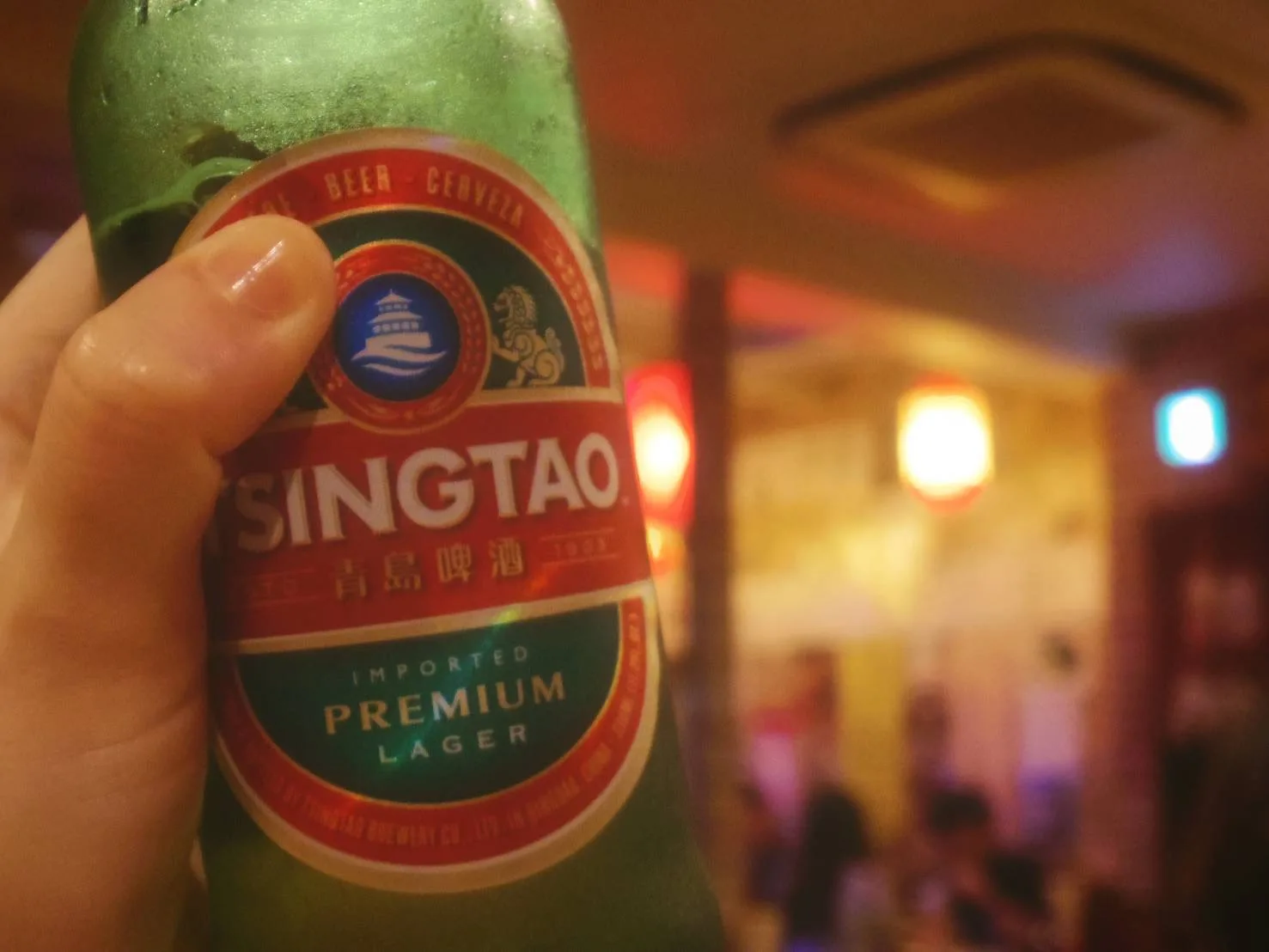 台湾料理店の店内で手に持った青島ビールの瓶