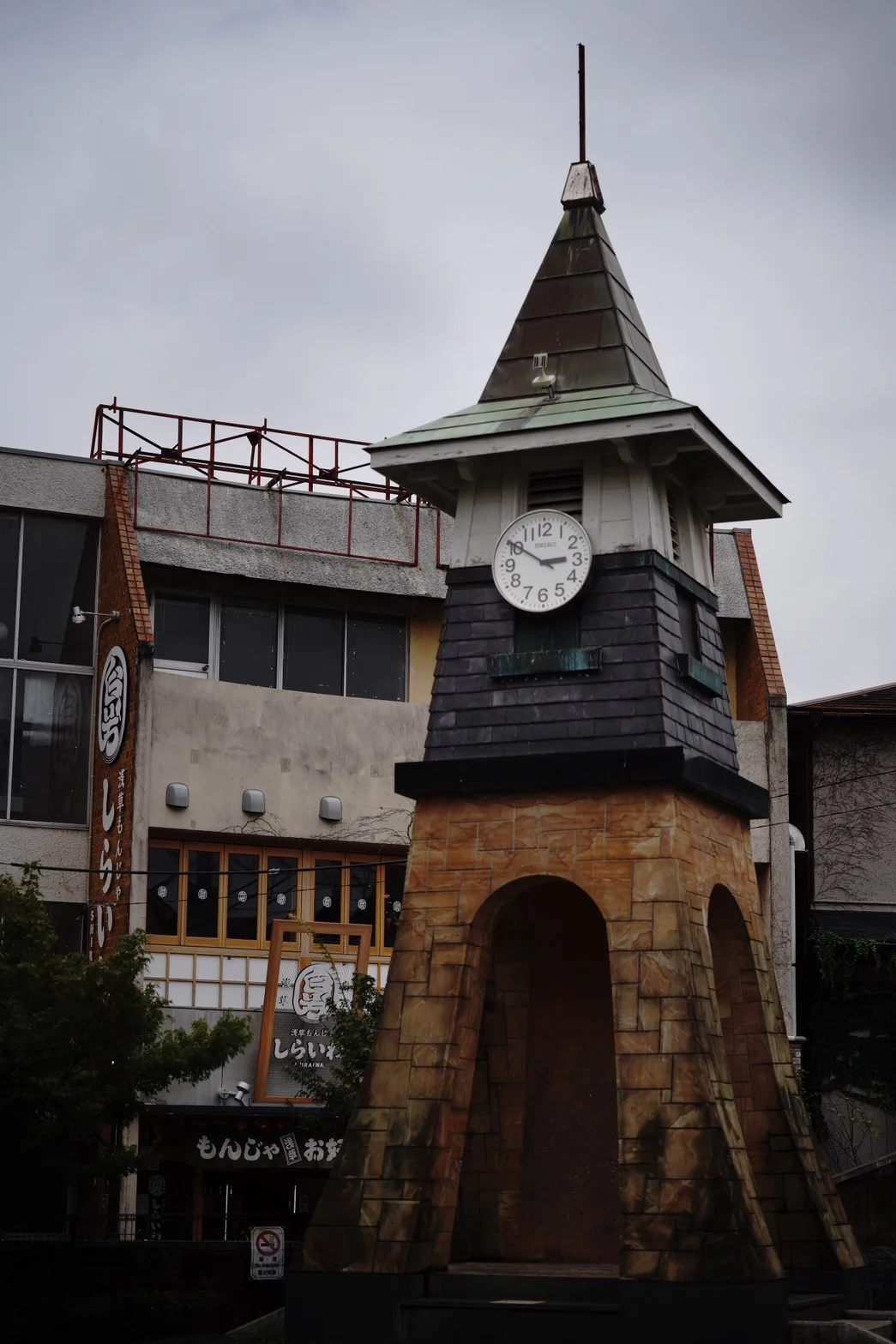 三角屋根に時計がついた塔と、その奥にもんじゃ焼きの看板を掲げた建物