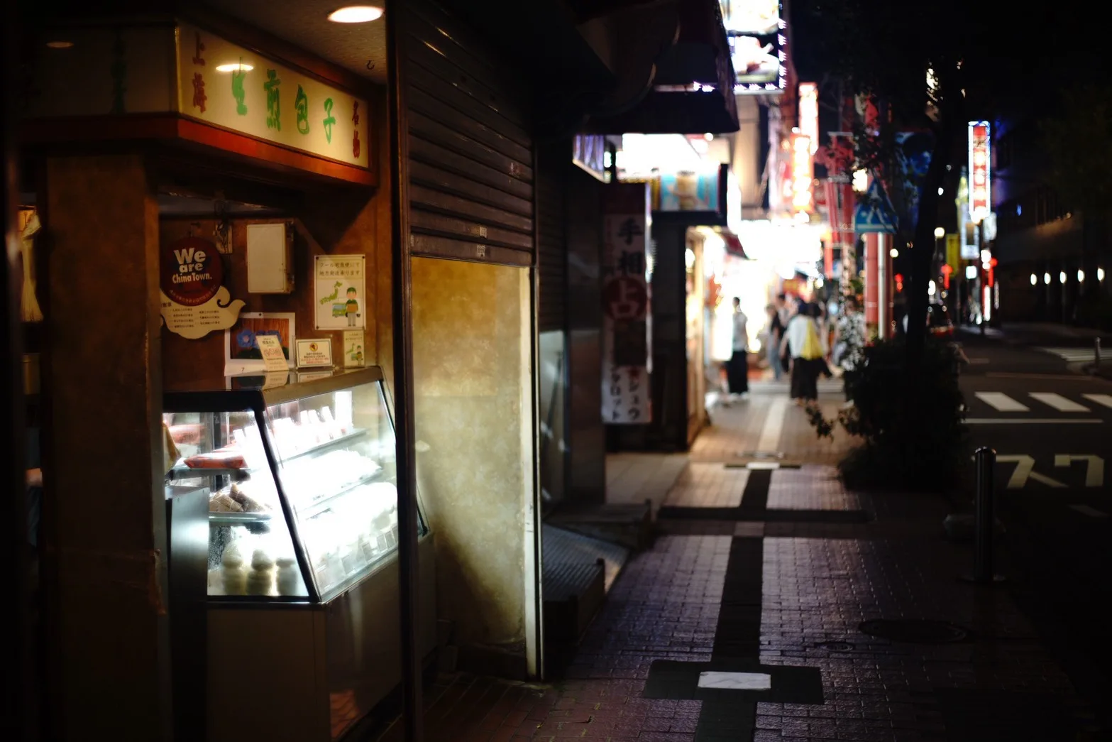 夜の中華街の路地。手前の店のショーケースの光と奥に続くネオン