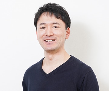 与えられた画像には、カメラに向かって微笑んでいる男性が写っています。彼は黒っぽいVネックのシャツを着ており、清潔感のある短髪で、真面目そうな印象を与えます。