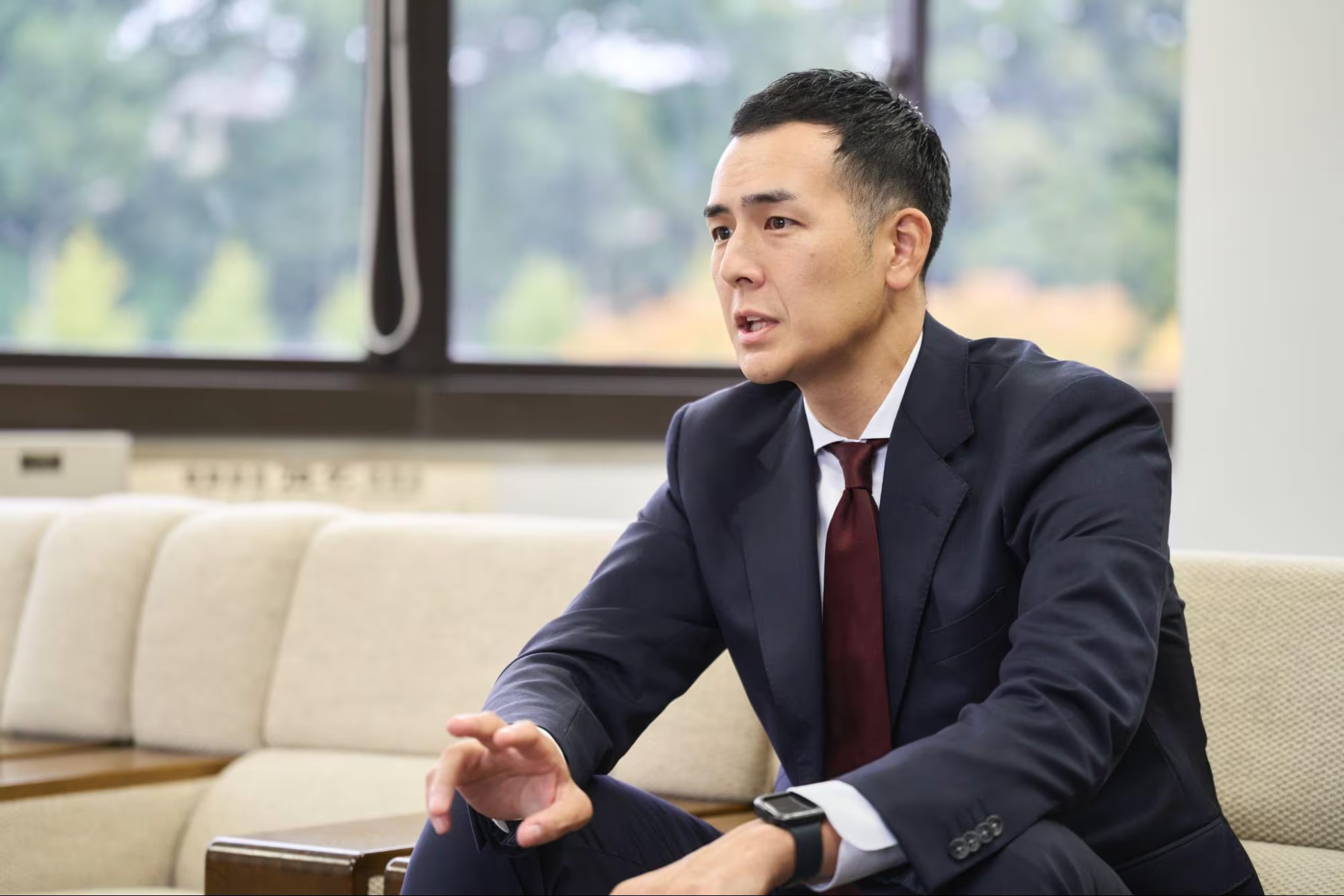 インタビュー中に身振り手振りで話すスーツ姿の男性。