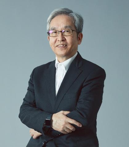 
眼鏡をかけ、腕を組んで微笑む壮年の男性のバストショット。