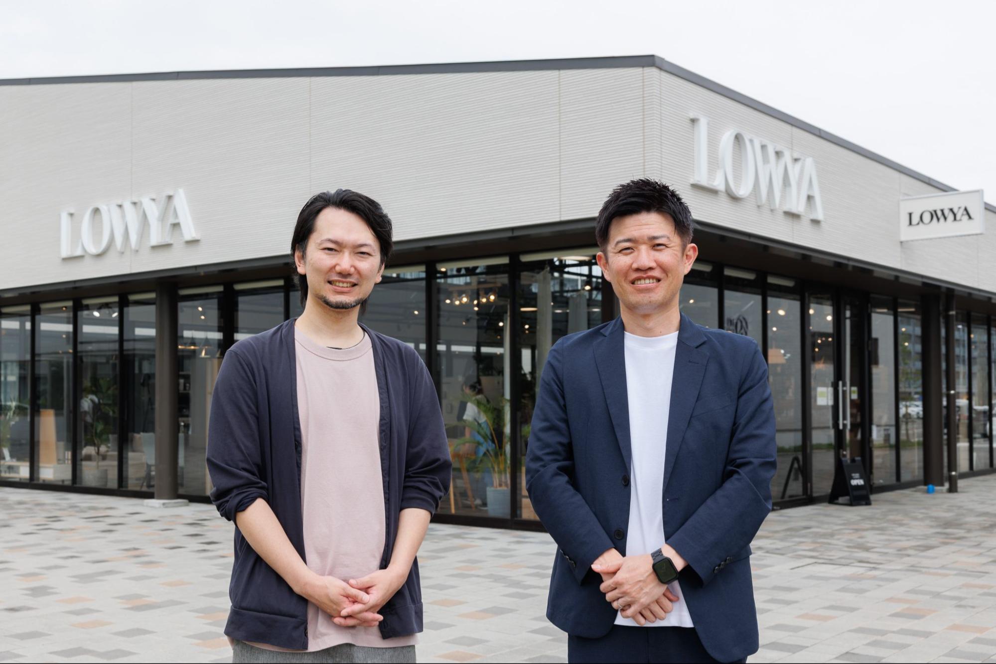 LOWYAの店舗前で微笑む2人の男性。一人はカジュアルな服装で、もう一人はジャケットを着用している。