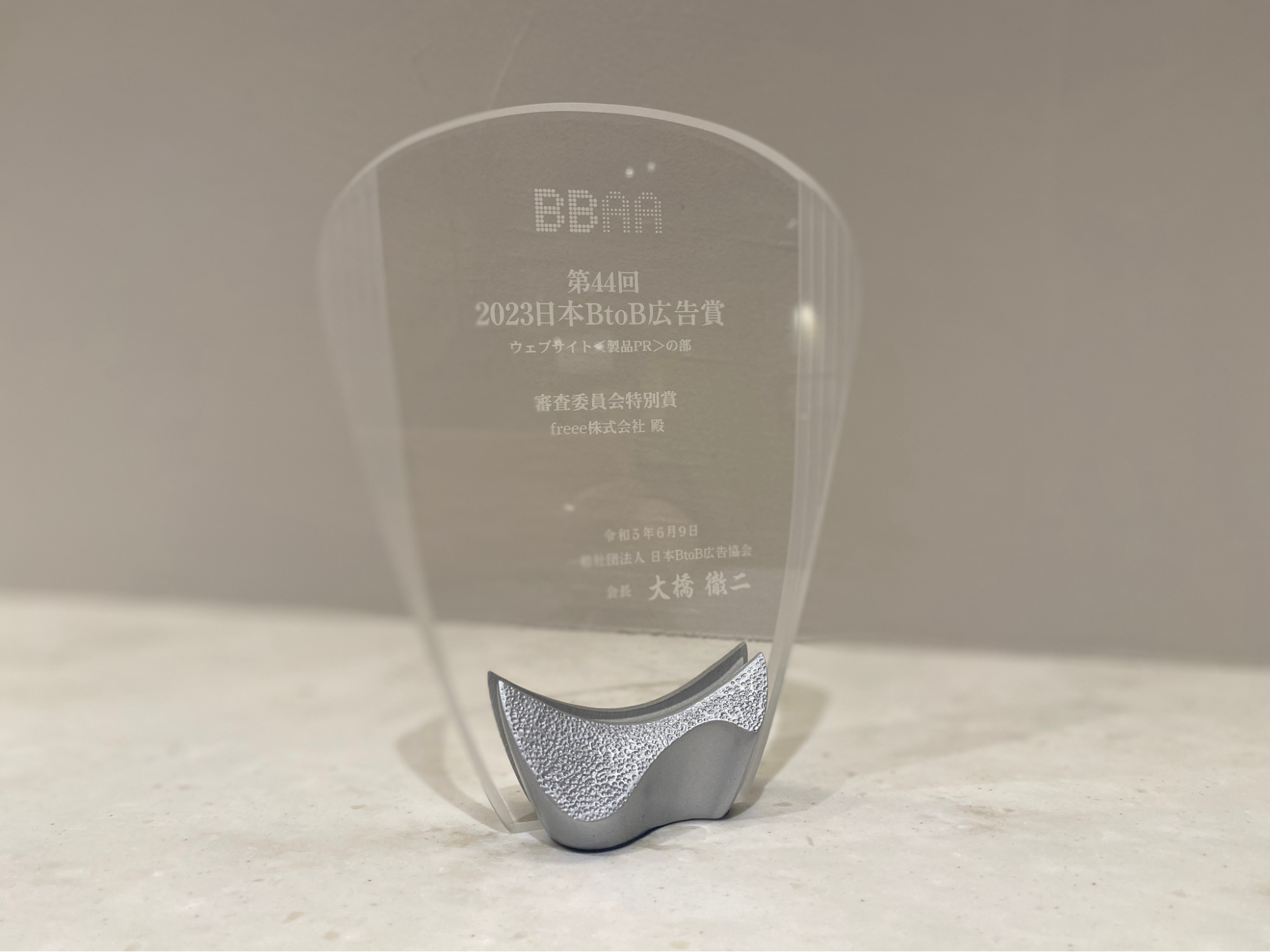 第44回BtoB広告賞において、審査委員会特別賞を受賞を記念したレリーフの写真。左右がせり上がっている銀色の土台（小さな挟み板）に、ガラス板が挟まれているレリーフ。受賞記念も文字が刻まれている。