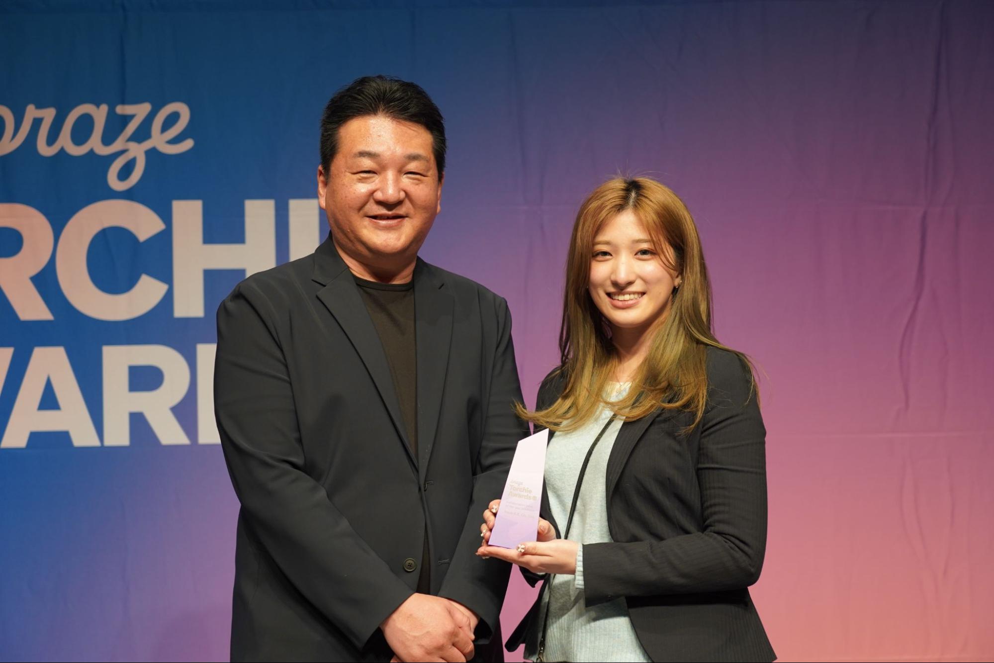 Braze Torchie Awardsの表彰状（トロフィー）を持つ女性とプレゼンターの記念写真。