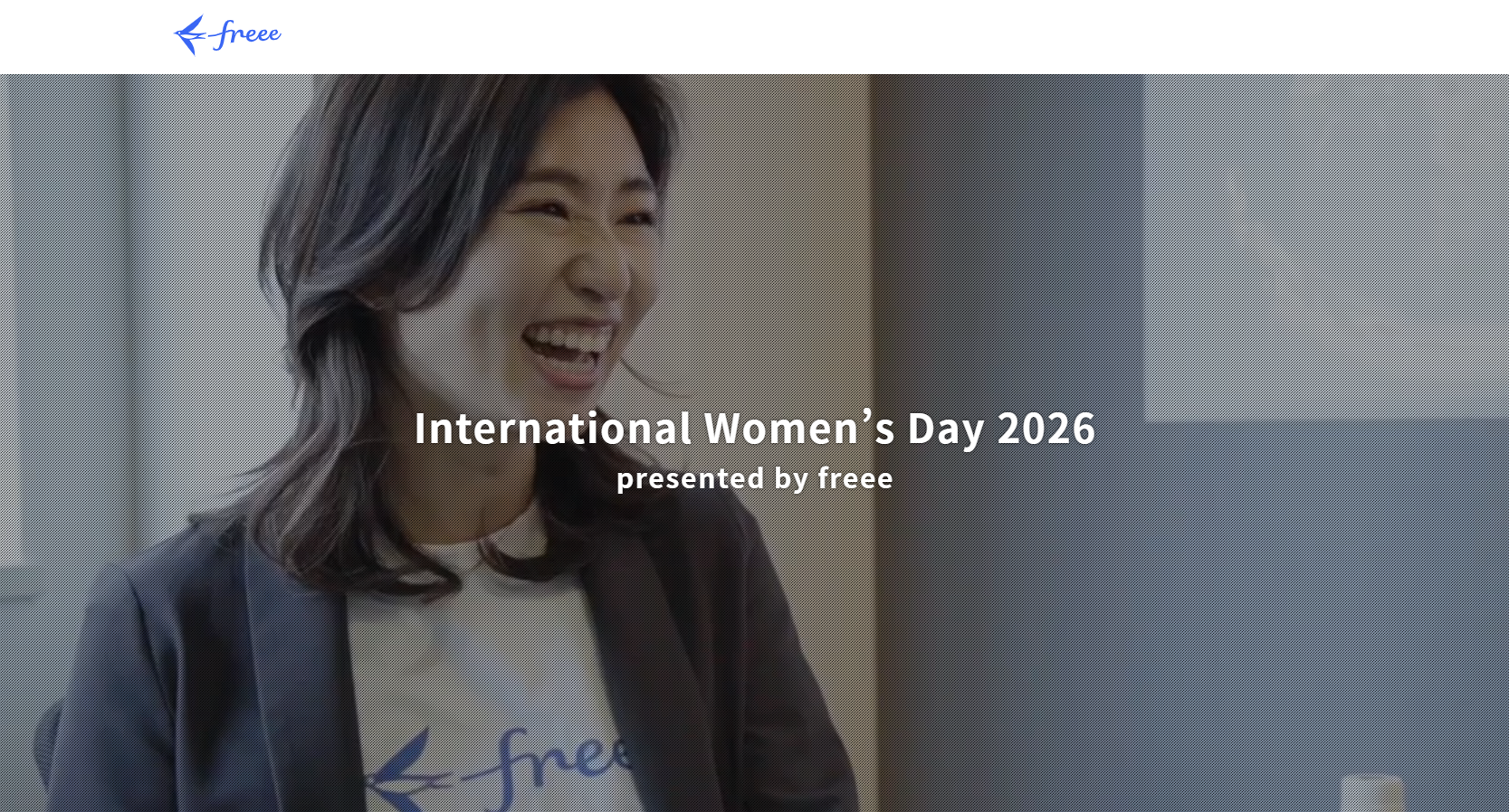 「International Women’s Day 2026 presented by freee」という白いテキストが中央に配置された画像。背景には、freeeのロゴ入りTシャツとジャケットを着用した女性が、明るい表情で笑いながら会話している様子が写っている。