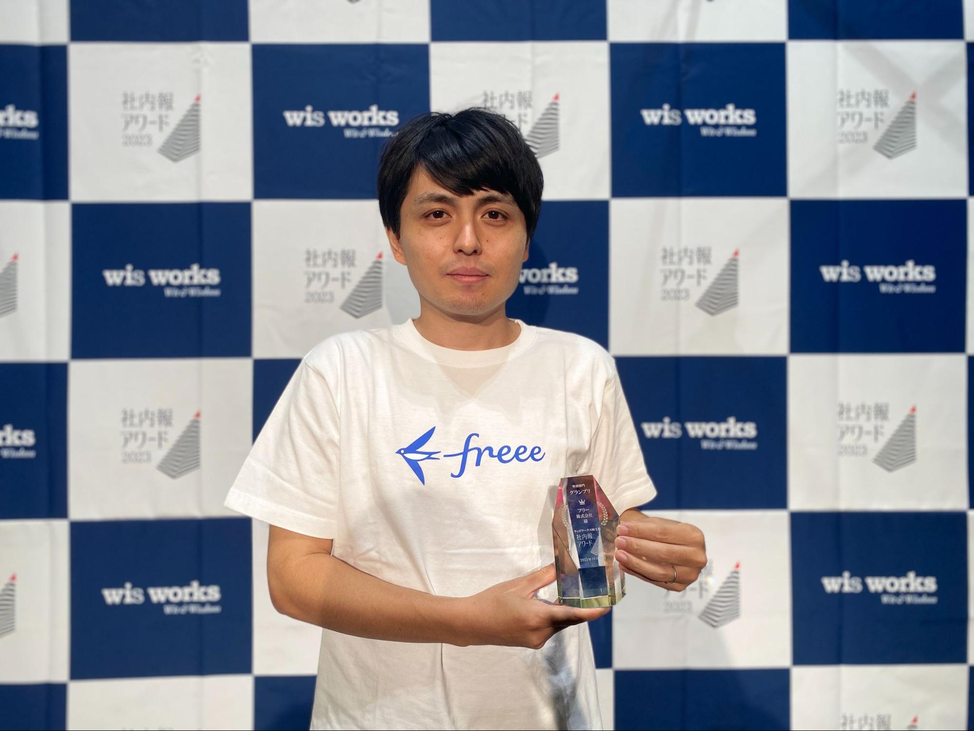 受賞トロフィーを手にした岡田さんの上半身写真。白のfreeeTシャツ着用。
