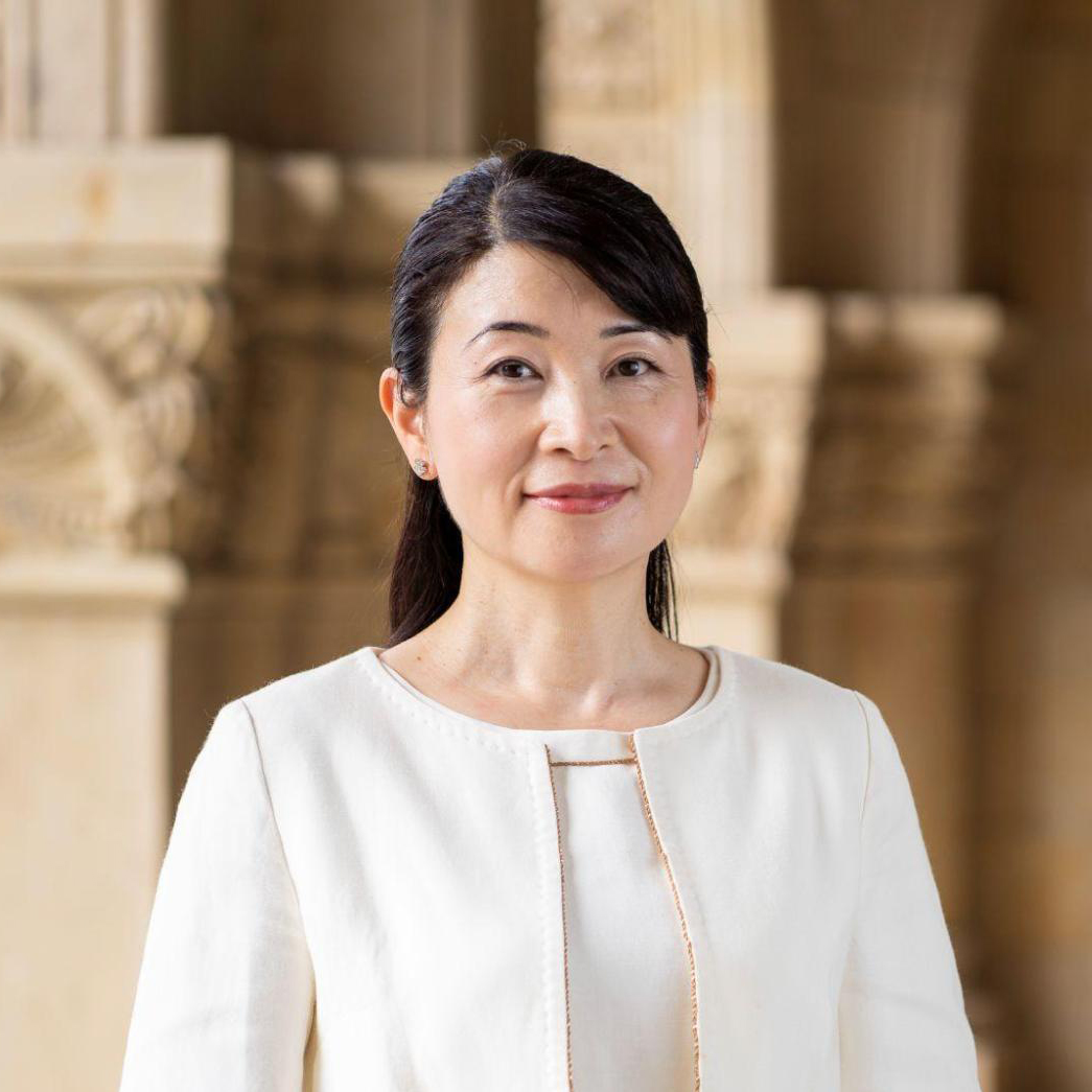 国立大学法人一橋大学 副学長／スタートアップ支援室長 西野和美氏のポートレート。一橋大学の校舎内を背景に、白いジャケットを着用して微笑んでいる。