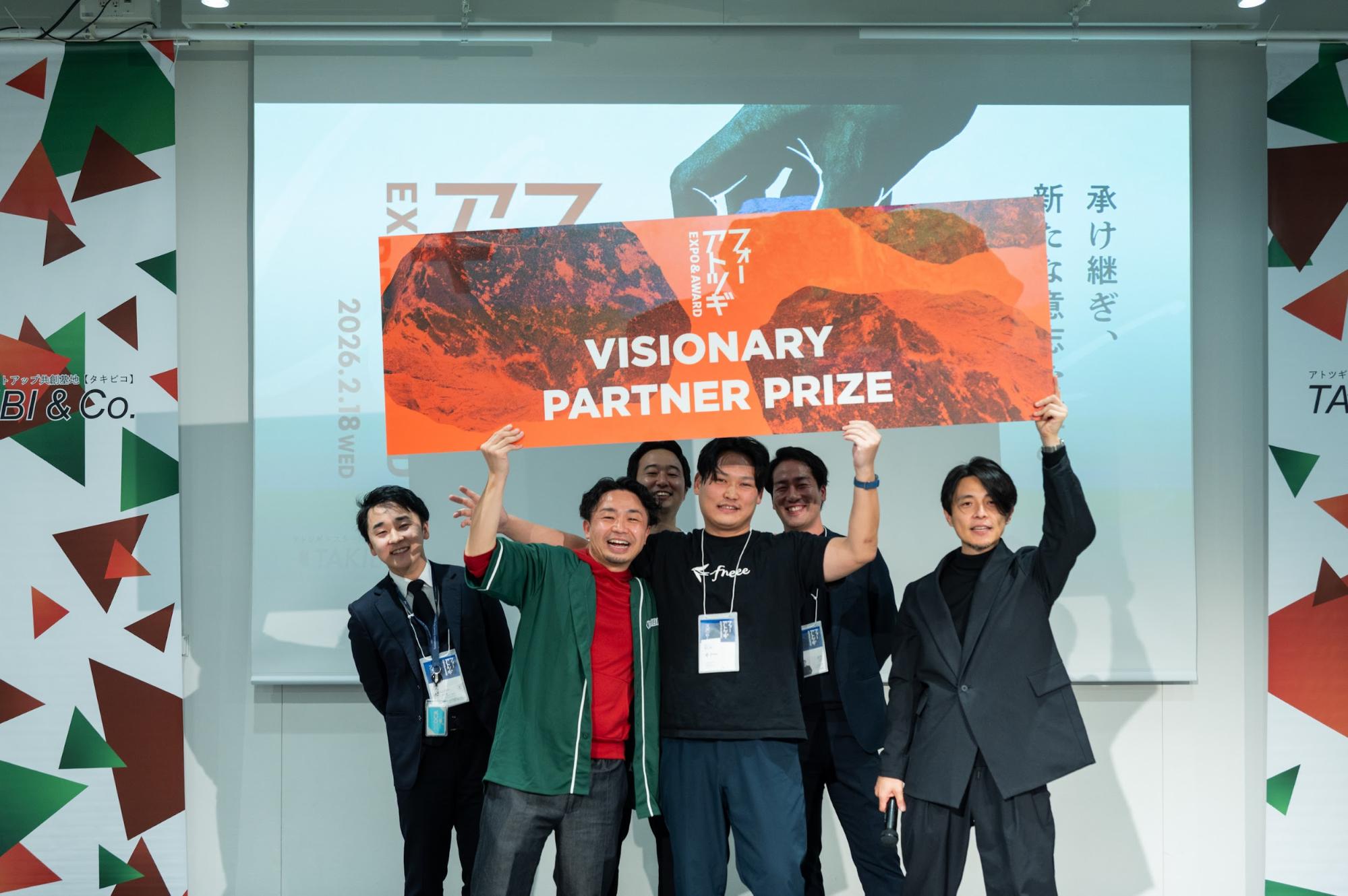 「フォーアトツギ EXPO & AWARD 2026」授賞式の様子。VISIONARY PARTNER PRIZEと書かれたオレンジ色のボードを掲げる受賞者たち。中央にはfreeeのTシャツを着たスタッフが笑顔で写っている。