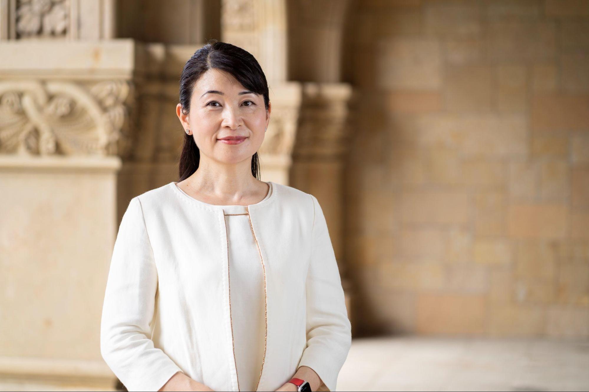 国立大学法人一橋大学 副学長／スタートアップ支援室長 西野和美氏のポートレート。一橋大学の校舎内を背景に、白いジャケットを着用して微笑んでいる。