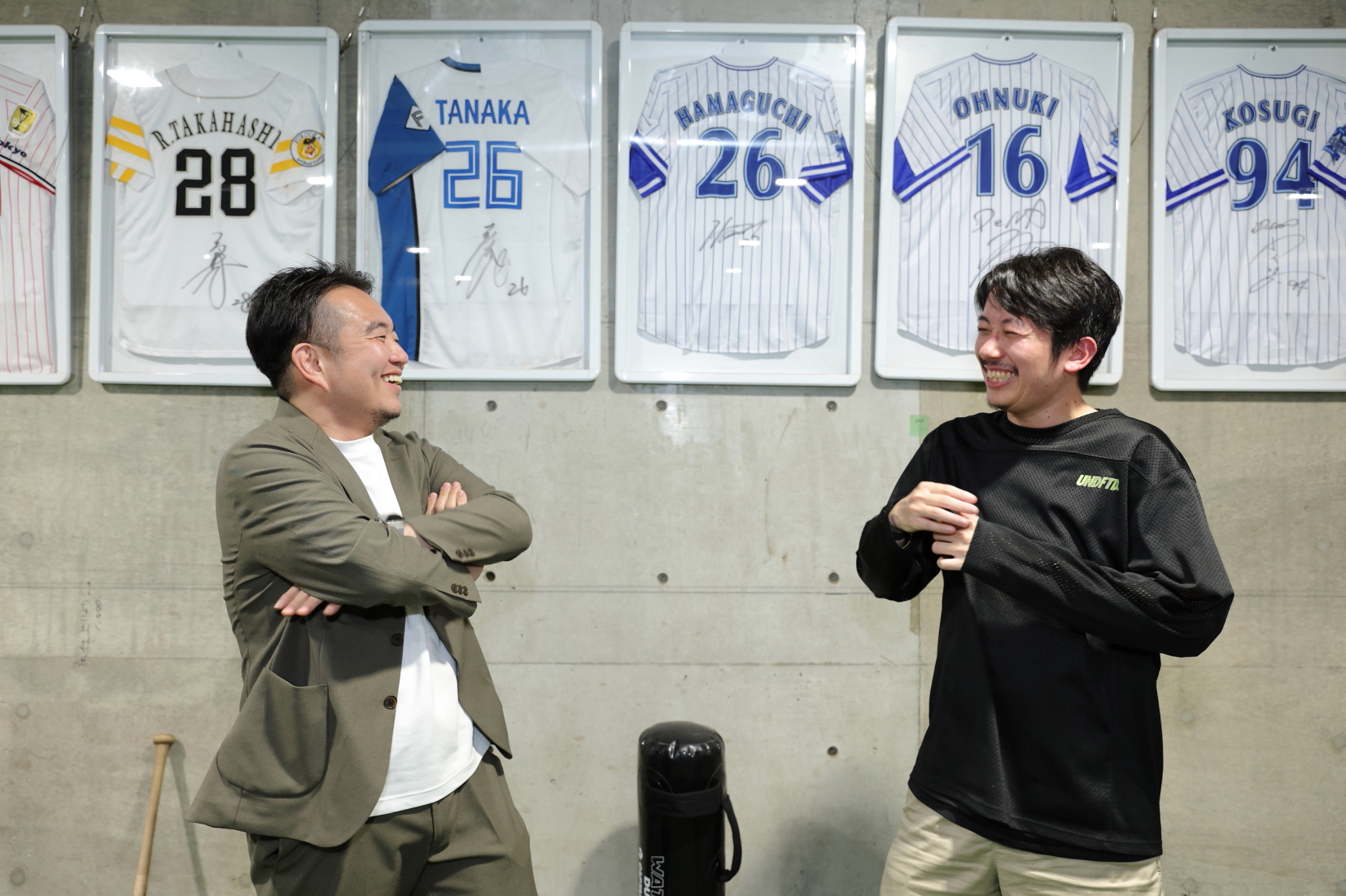 二人の背景にはプロ野球選手たちのユニフォームが並ぶ