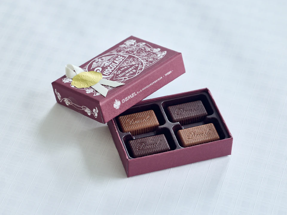 デメルの『ソリッドチョコレート』。赤紫色の小箱の中に4つのチョコレートが入っている。蓋には白一色でデザインが施されており、金色のシールとリボンが貼られている。