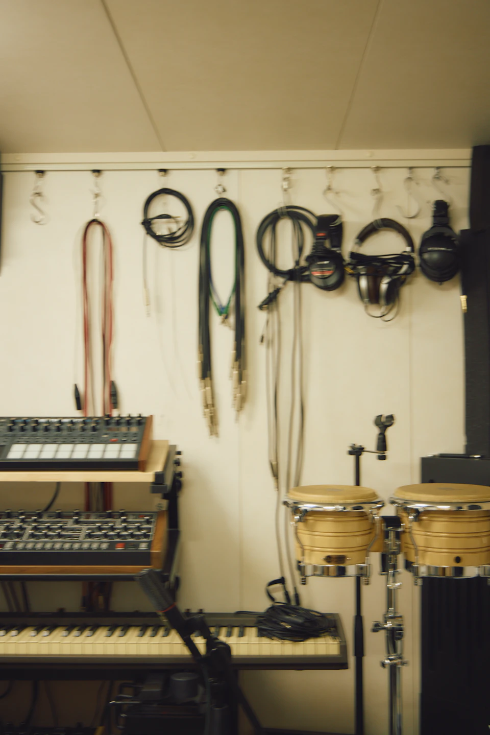 tofubeatsさんの作業部屋の一角。壁に沿って楽器が置かれており、壁の天井付近に付けられたフックには、ヘッドホンやコードの数々が掛けられている。