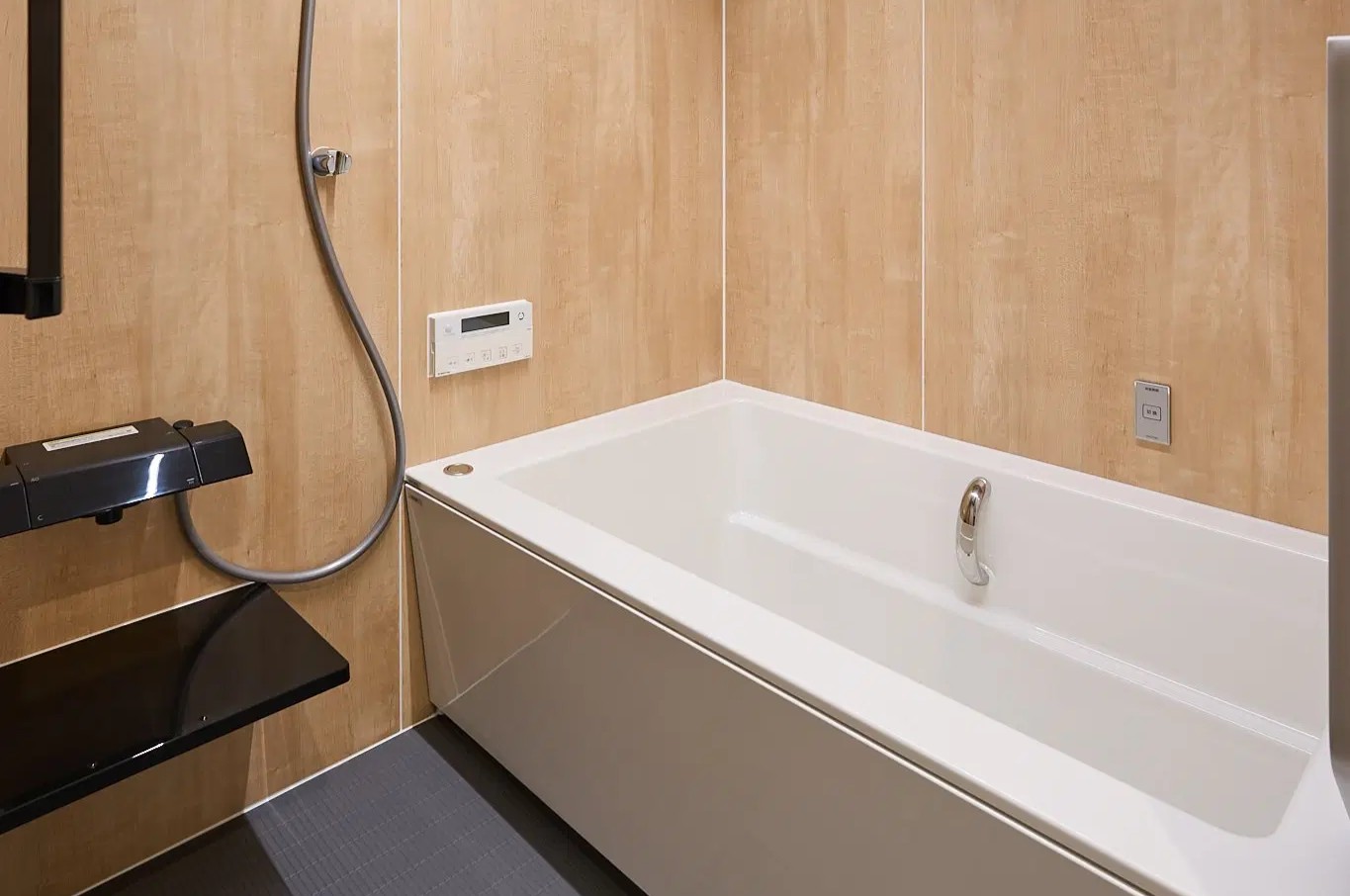 木目調の壁パネルとブラックの床が落ち着いた和モダンの雰囲気を演出する浴室。清潔感のある白い浴槽を組み合わせ、京都のマンションで旅館のようなくつろぎ気分を味わえる空間に仕上げた。ANRI STYLE/リノベ図書館の施工事例。