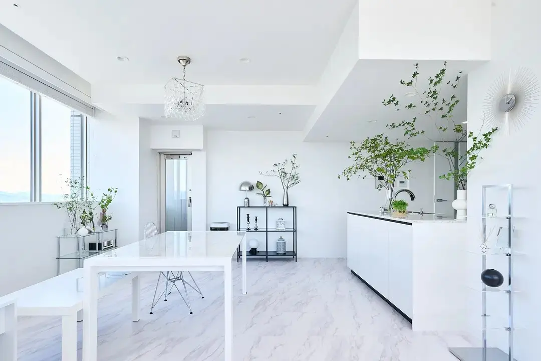 白を基調としたLDKの写真。床は大理石調のタイル張りで、白いダイニングテーブルと白いアイランドキッチンが置かれている。