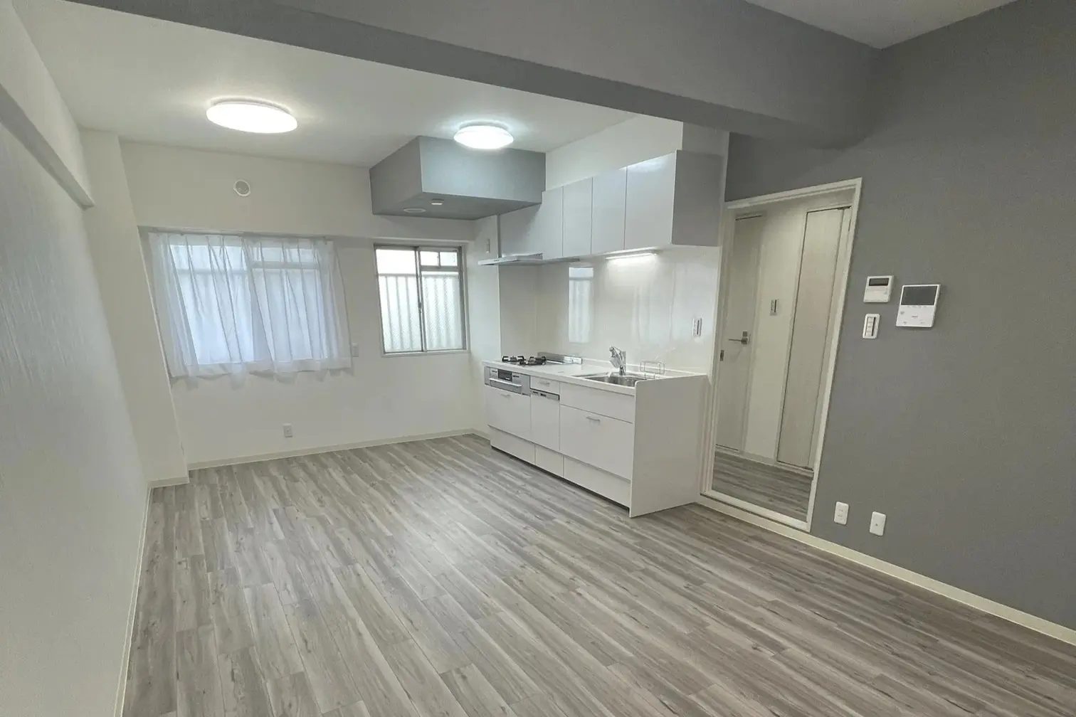 リフレネクスト横浜の事例。白とグレーで統一されたシンプルで上品なLDK。壁付けの白いキッチンとグレーのクロスが調和し、間仕切りを撤去して開放感を創出。幅広い層に向けデザインされた、築40年マンションのフルリノベーション内観