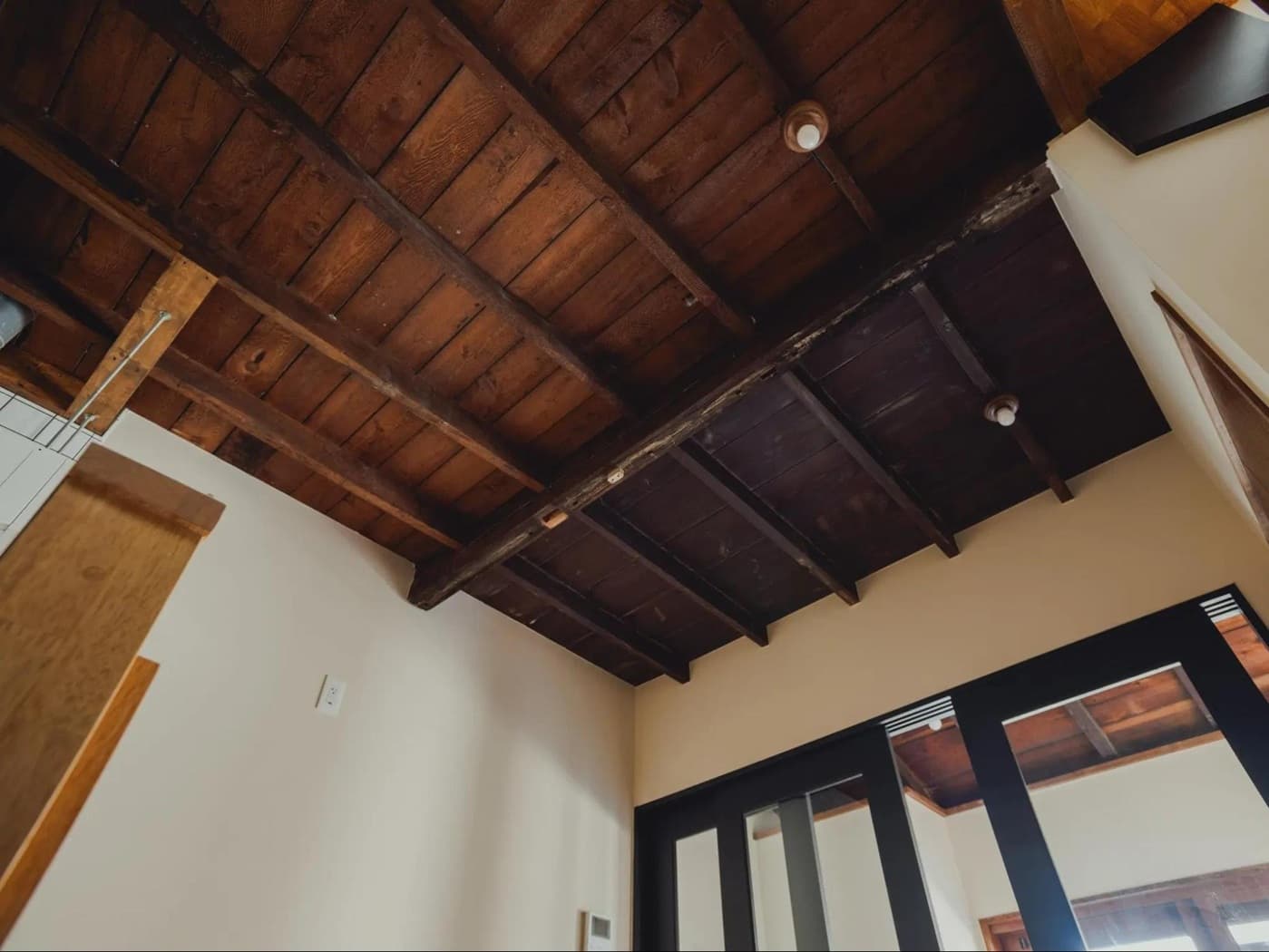 アズ建設による築100年の長屋リノベーション事例。既存の古い梁や天井板をダークブラウンに塗装してあえて見せ、白い壁と対比させた開放的で趣のある天井空間。